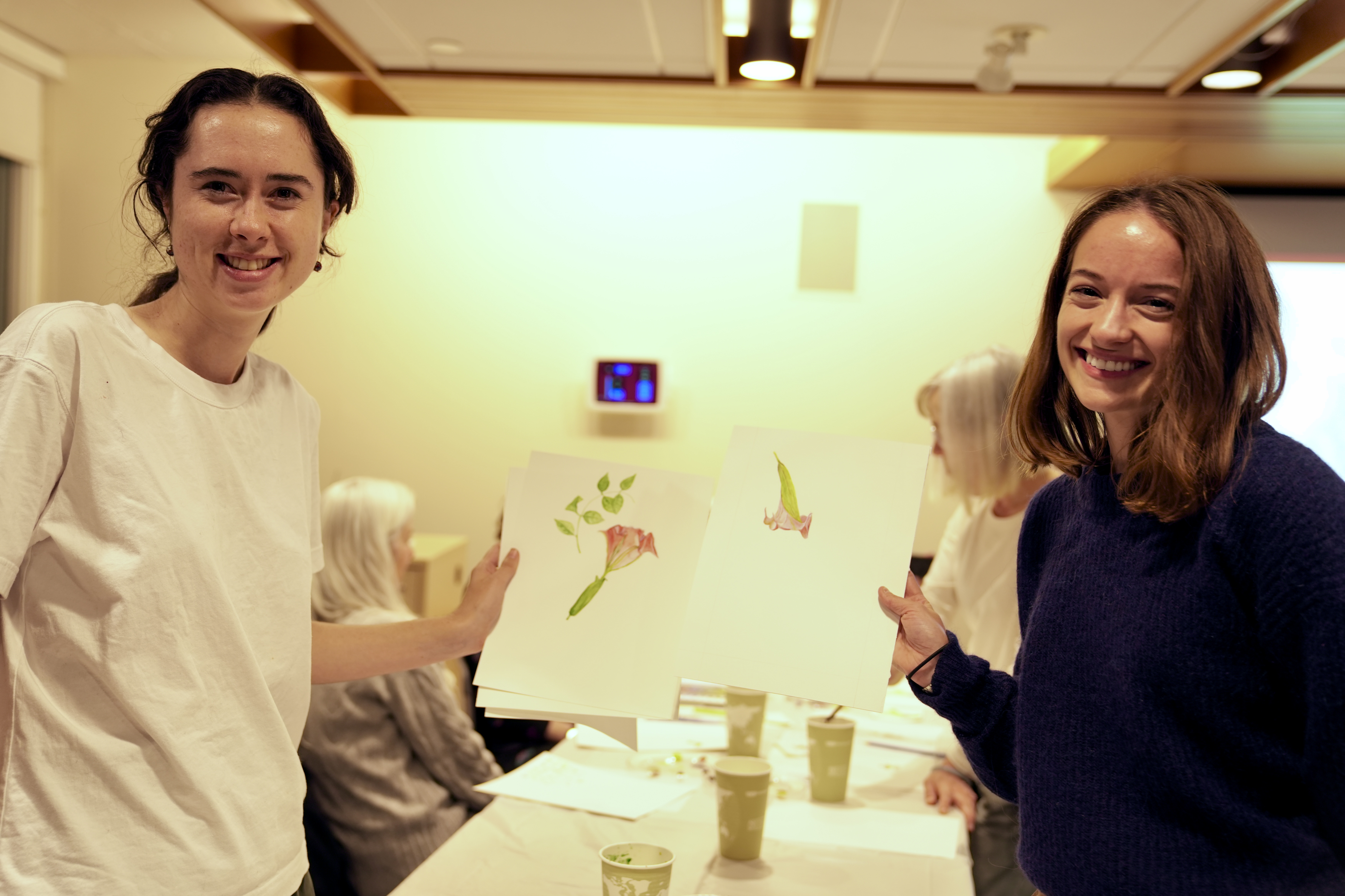 Two workshop participants, smiling holding their paintings up