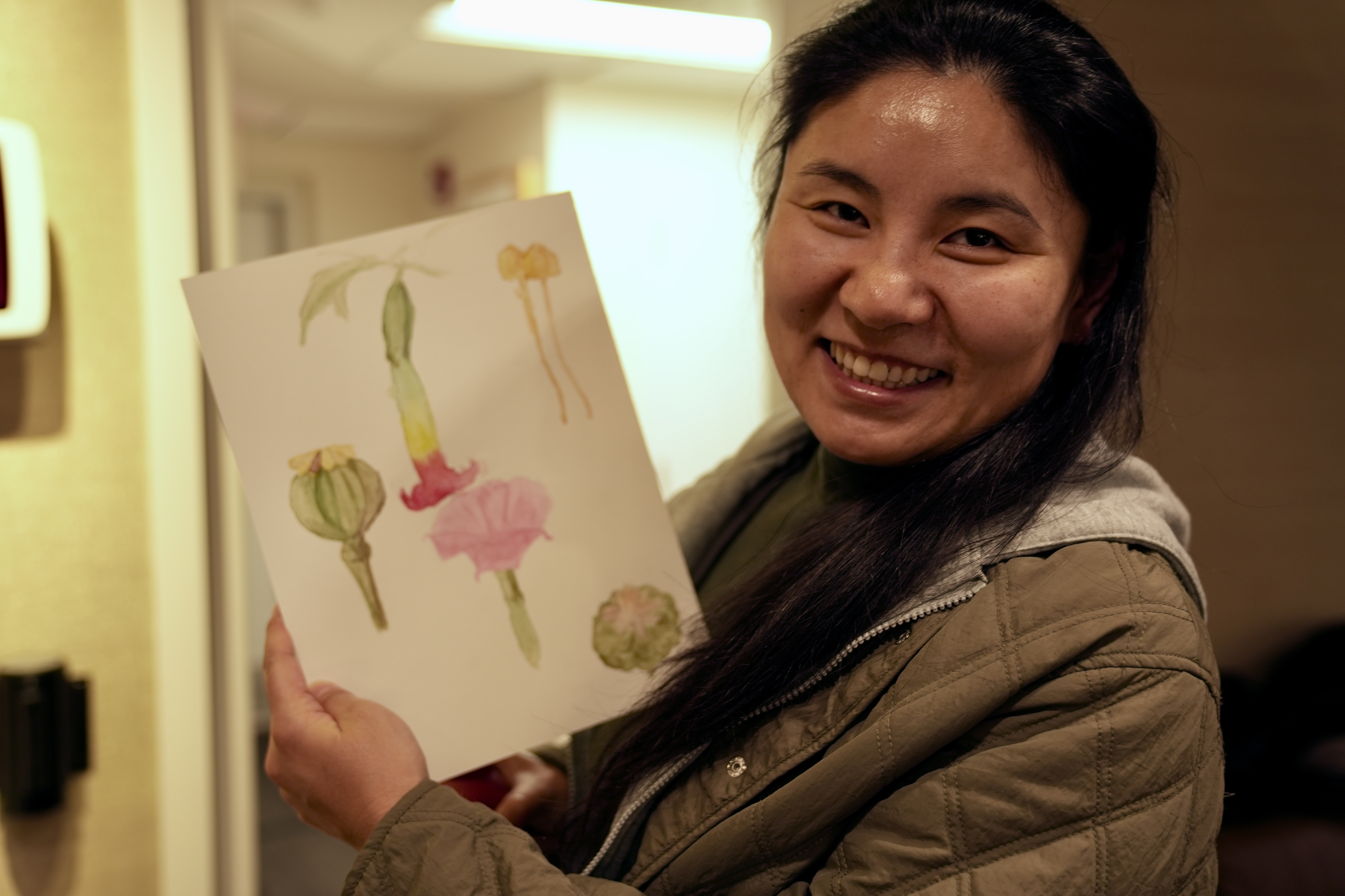 workshop participant holds paper of botanical painting and smiles
