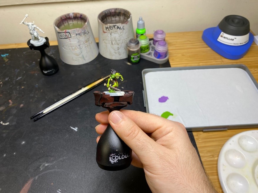 Hand holding Warhammer figurine, paints and brushes in the background