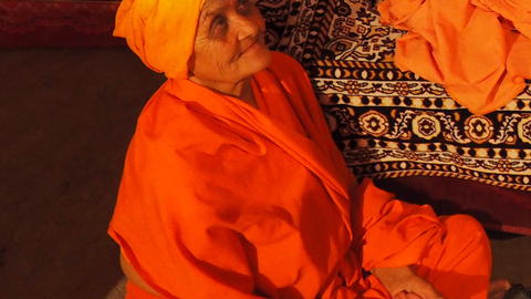 Woman in orange robes and head scarf seated cross-legged looking up
