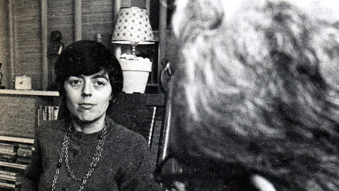 Jane Roberts seated in a chair in an office looking towards a man taking notes.