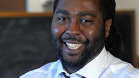 Biko Mandela Gray wearing a white shirt and black tie looks at camera smiling