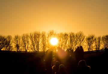 Sunset on the horizon, bare trees and some outlines of people in the foreground
