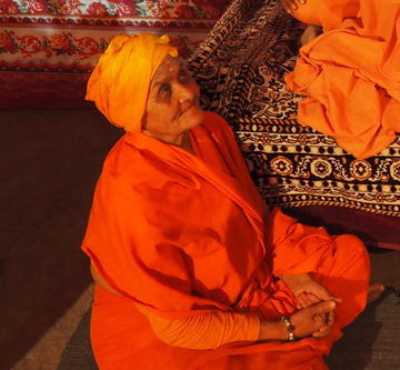 Woman in orange robes and head scarf seated cross-legged looking up