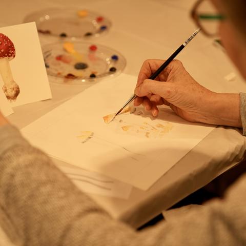close up of workshop participant's hands painting mushroom 