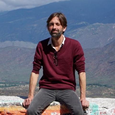 Professor Hugh Urban sitting on a wall, mountains in the background