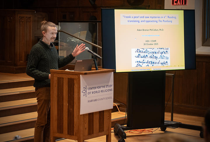 Adam Bremer-McCollum at the podium gesturing towards the monitor