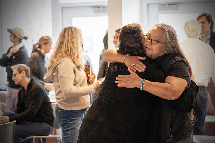 Two individual in an embrace, others in the background talking