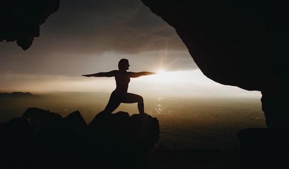 In profile someone practicing yoga with sunrise or sunset in the background.