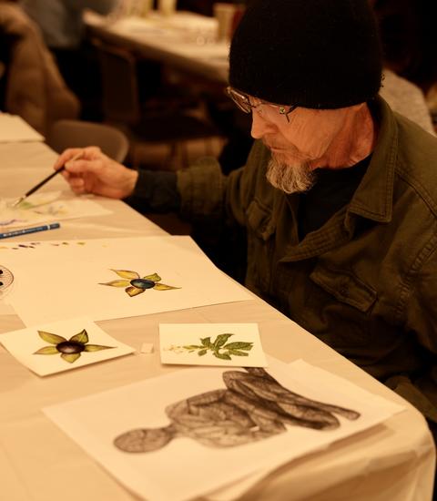 bearded man sits at table and holds paint brush