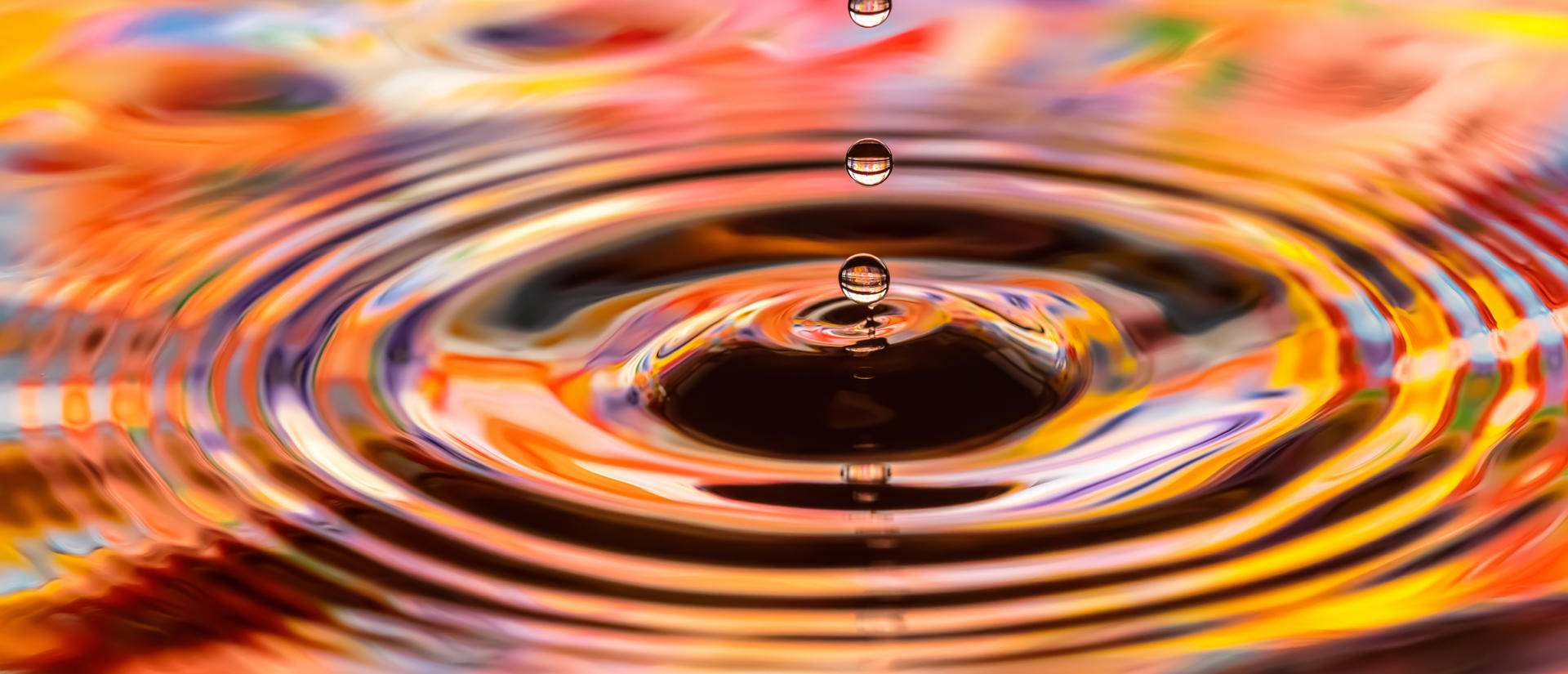 Drops falling onto a pool of water with colors reflecting off of the water