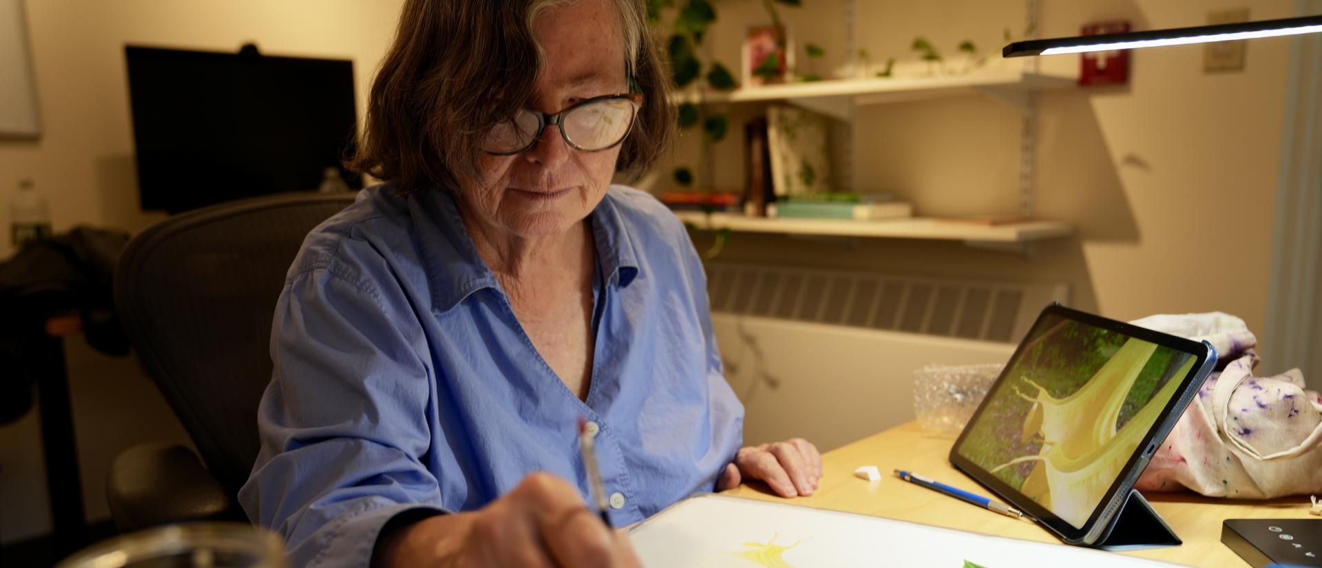 Donna Torres at her desk placing a brush into a pallet of paint