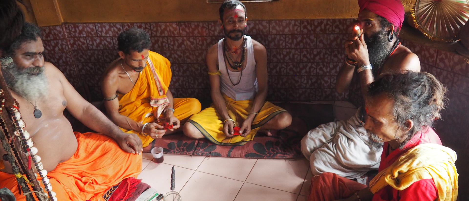 men seated in a circle, one smoking a pipe