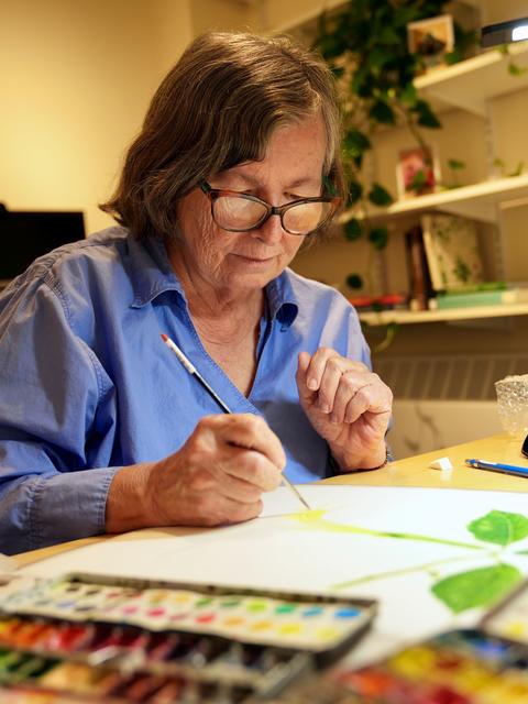 Donna Torres seated at her desk painting a flower