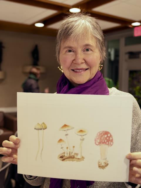 woman smiles and holds painting of 5 mushrooms