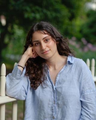 Emma Scharff leaning against a white picket fence smiling into the camera