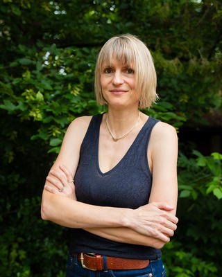 Ulrike Wagner, arms crossed standing outside in front of trees, smiling into the camera
