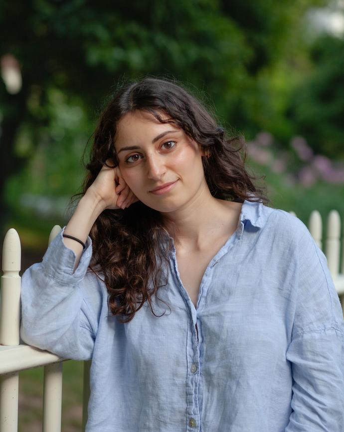 Emma Scharff leaning against a white picket fence smiling into the camera