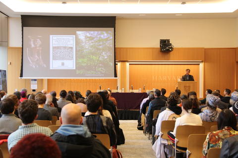 Photo of conference attendees seated facing presenter and screen